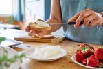 Woman making summer strawberry sandwich. Female hands spread stracchino cheese on bread for toast. Healthy eating, fruit dieting brunch.